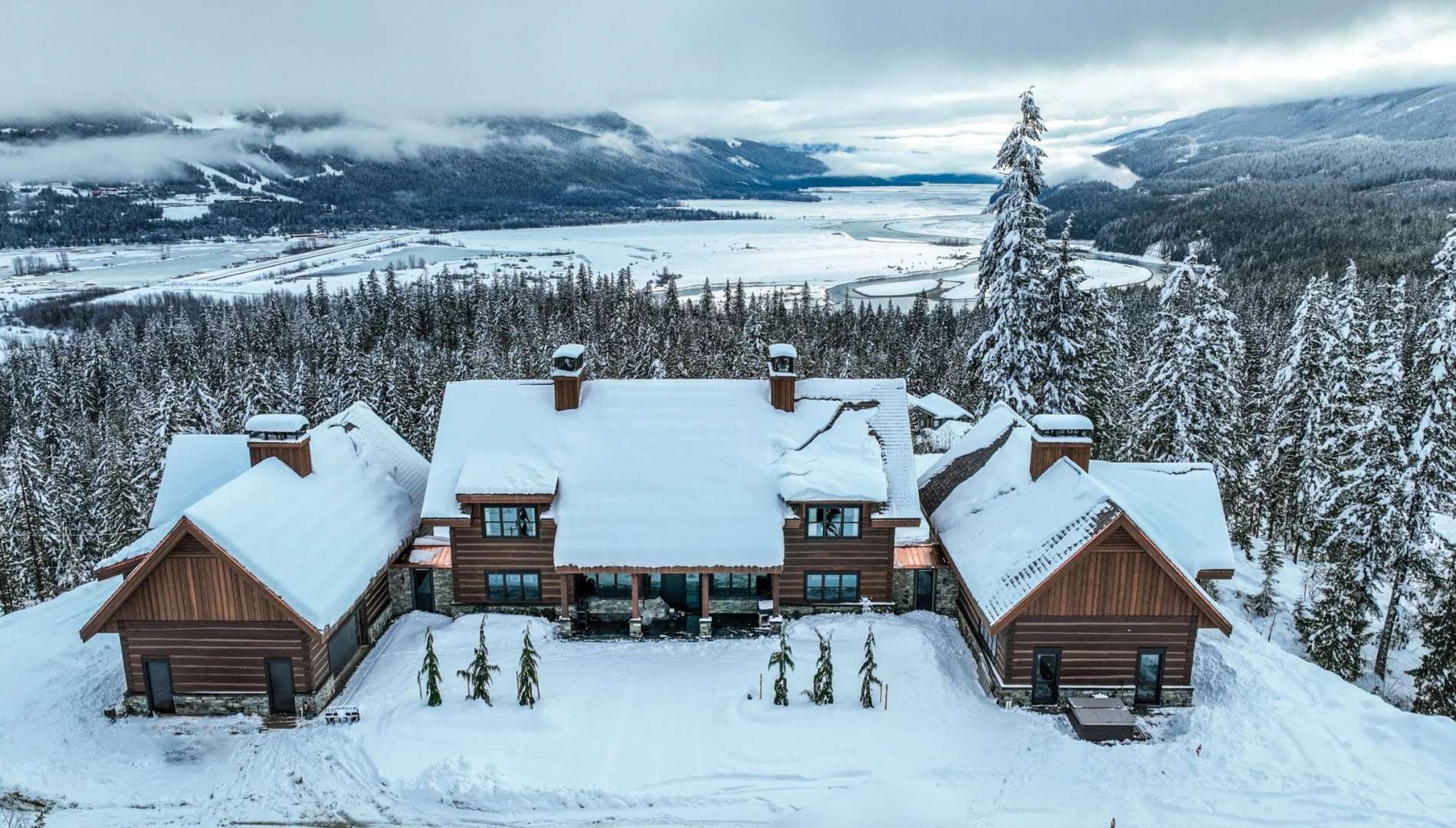 Douglas Fir dovetail log home in Revelstoke, BC with snow-covered gable roofs, stone accents, and mountain valley views