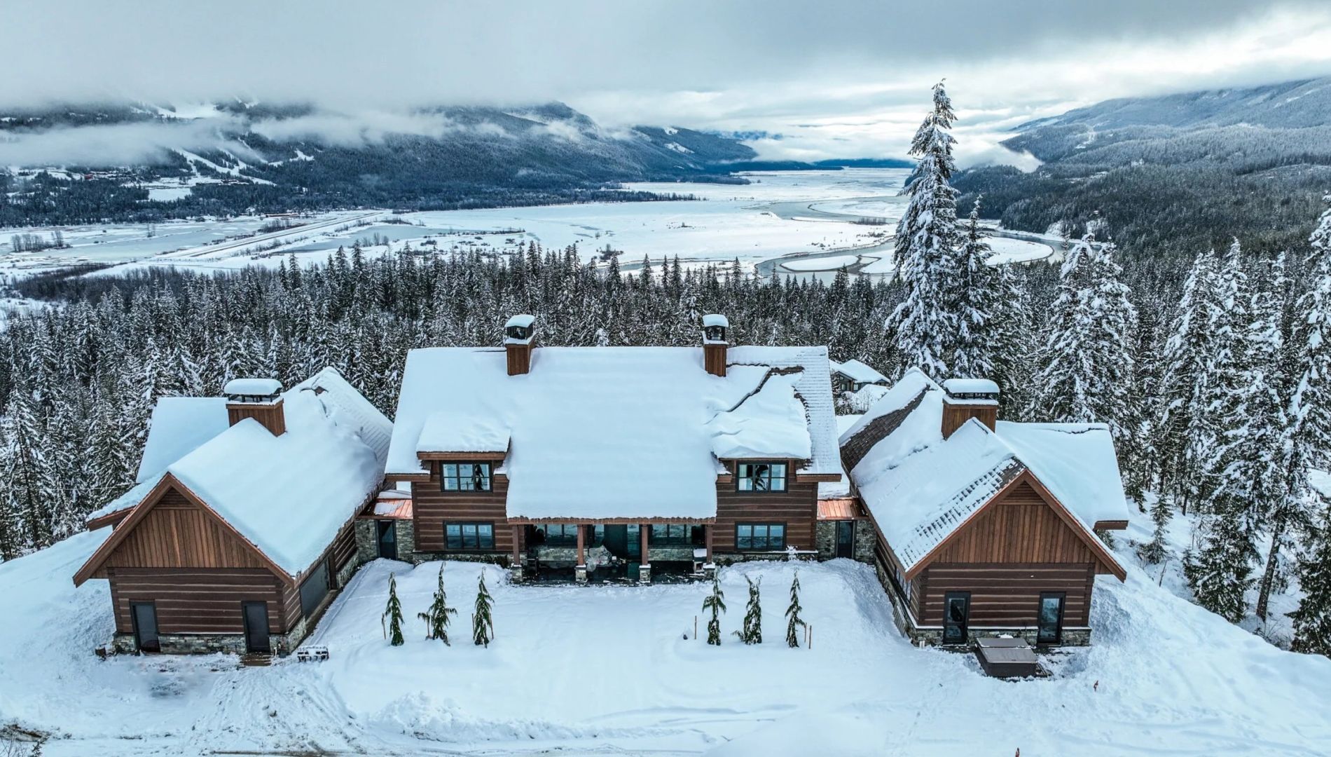 Douglas Fir dovetail log home in Revelstoke, BC with snow-covered gable roofs, stone accents, and mountain valley views
