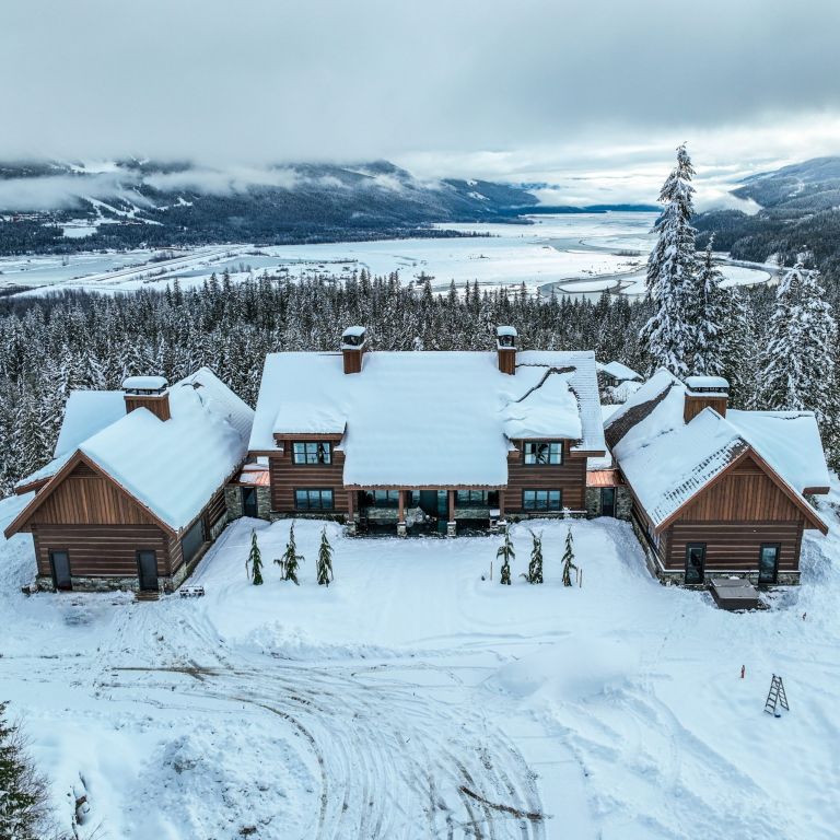 Douglas Fir dovetail log home in Revelstoke, BC with snow-covered gable roofs, stone accents, and mountain valley views