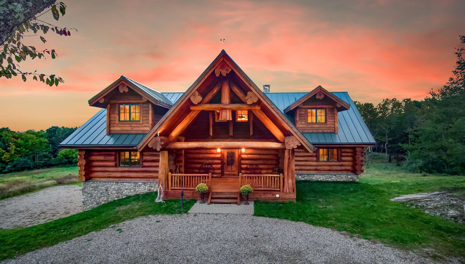 Western Red Cedar log home in Connecticut with metal roof, dormers, river rock foundation, and exposed log truss entry