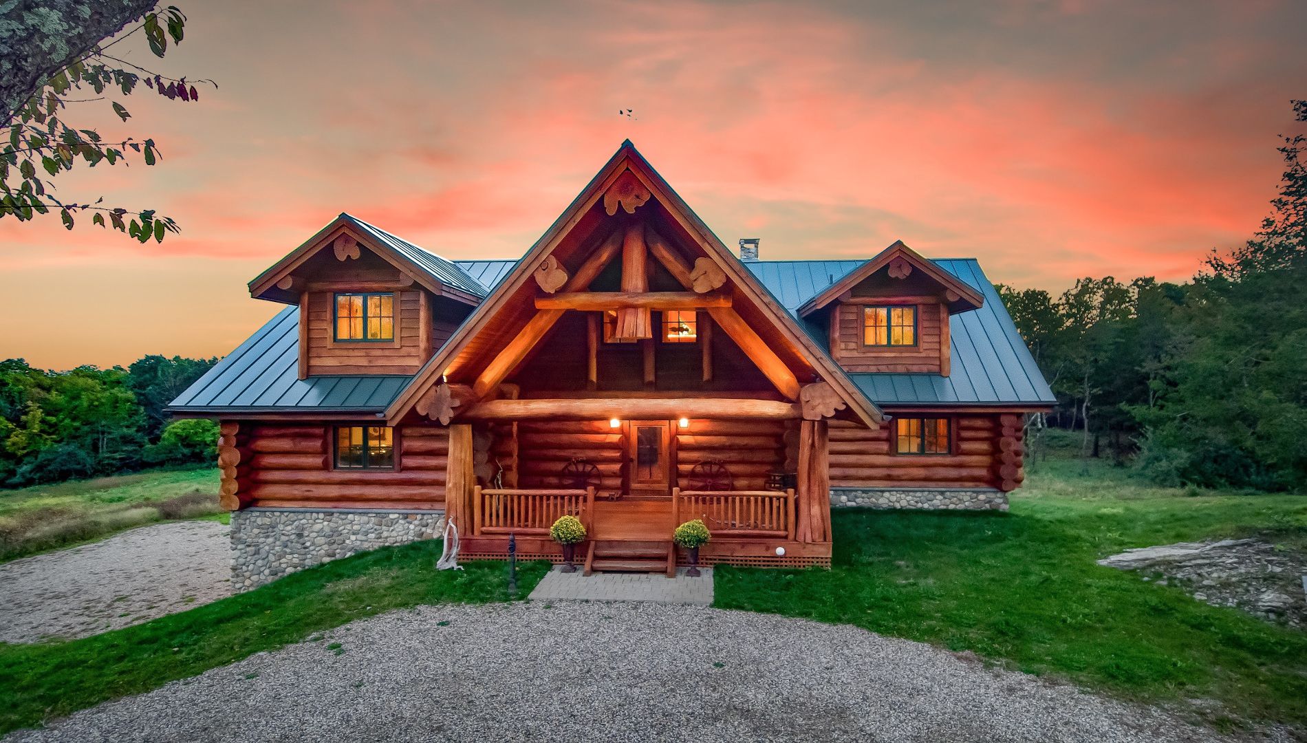 Western Red Cedar log home in Connecticut with metal roof, dormers, river rock foundation, and exposed log truss entry