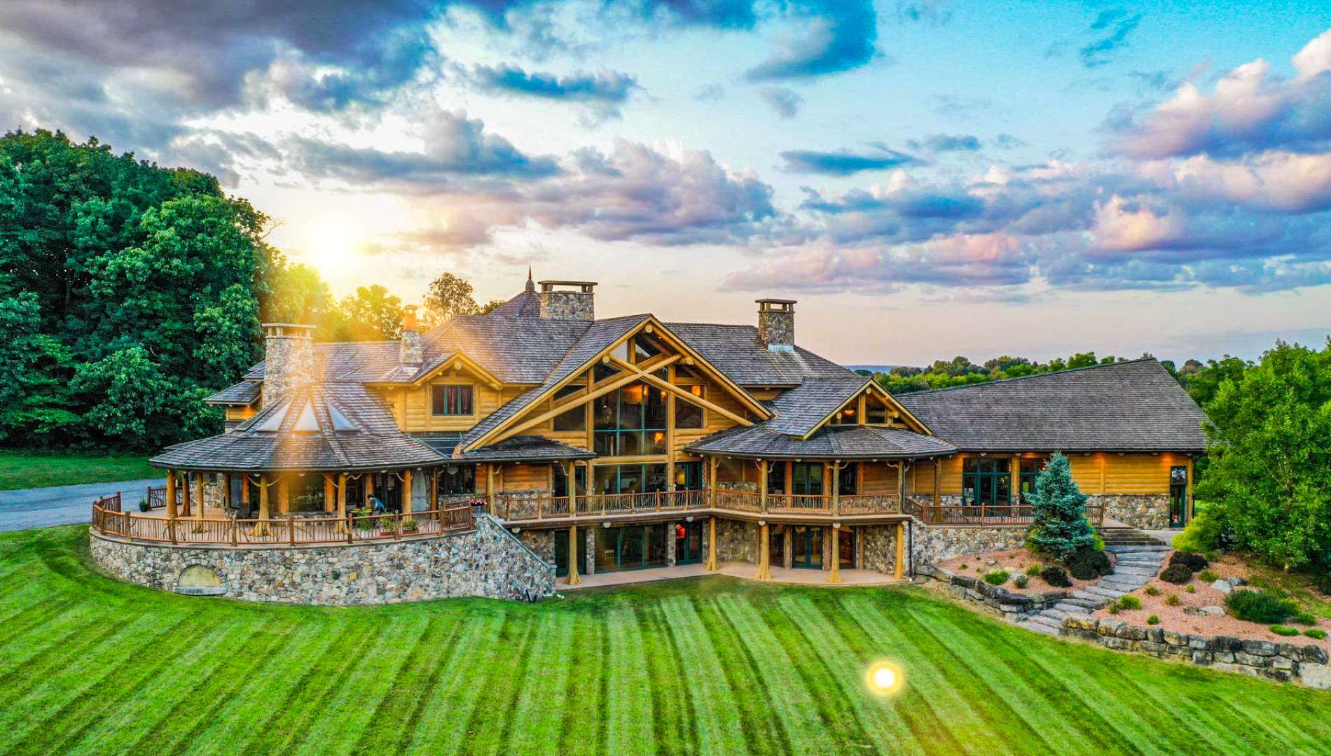 Large Douglas Fir post and beam home in Pennsylvania with cedar shake roof, stone foundation, wraparound deck, and sunset lighting