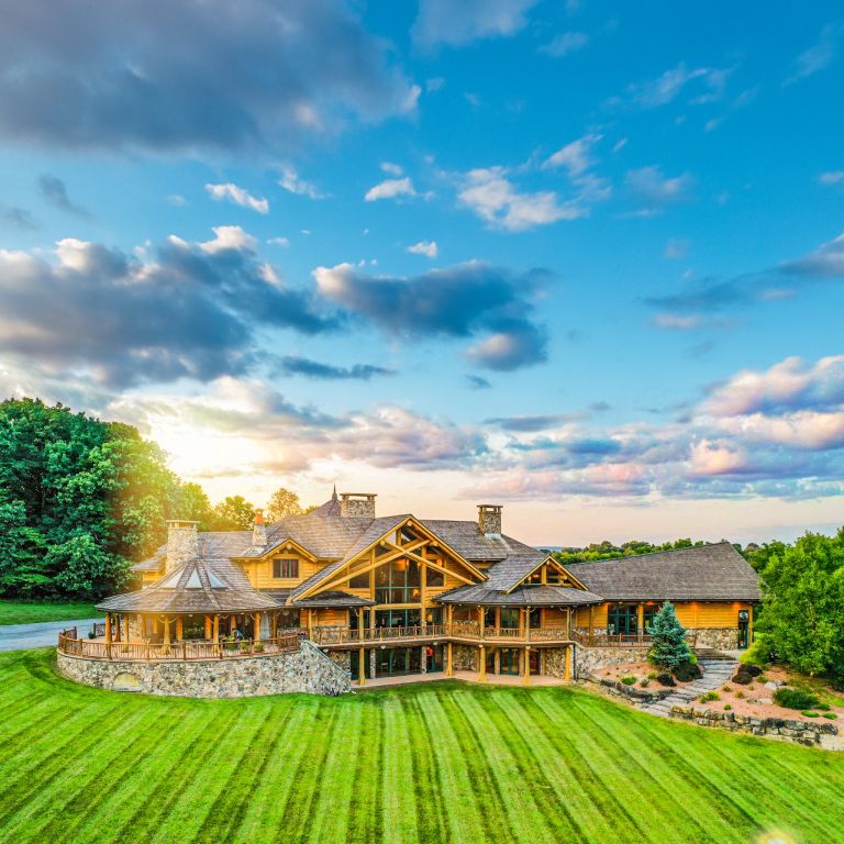 Large Douglas Fir post and beam home in Pennsylvania with cedar shake roof, stone foundation, wraparound deck, and sunset lighting