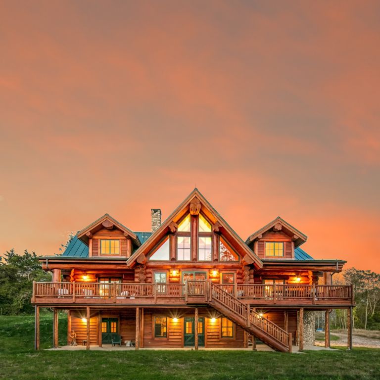Western Red Cedar log home in Connecticut with green metal roof, large deck, A-frame windows, and sunset sky backdrop