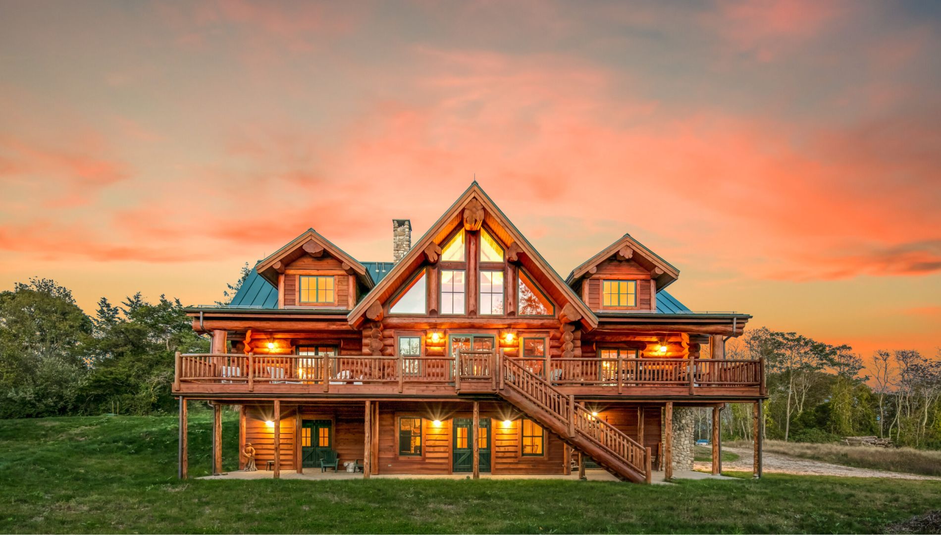 Western Red Cedar log home in Connecticut with green metal roof, large deck, A-frame windows, and sunset sky backdrop