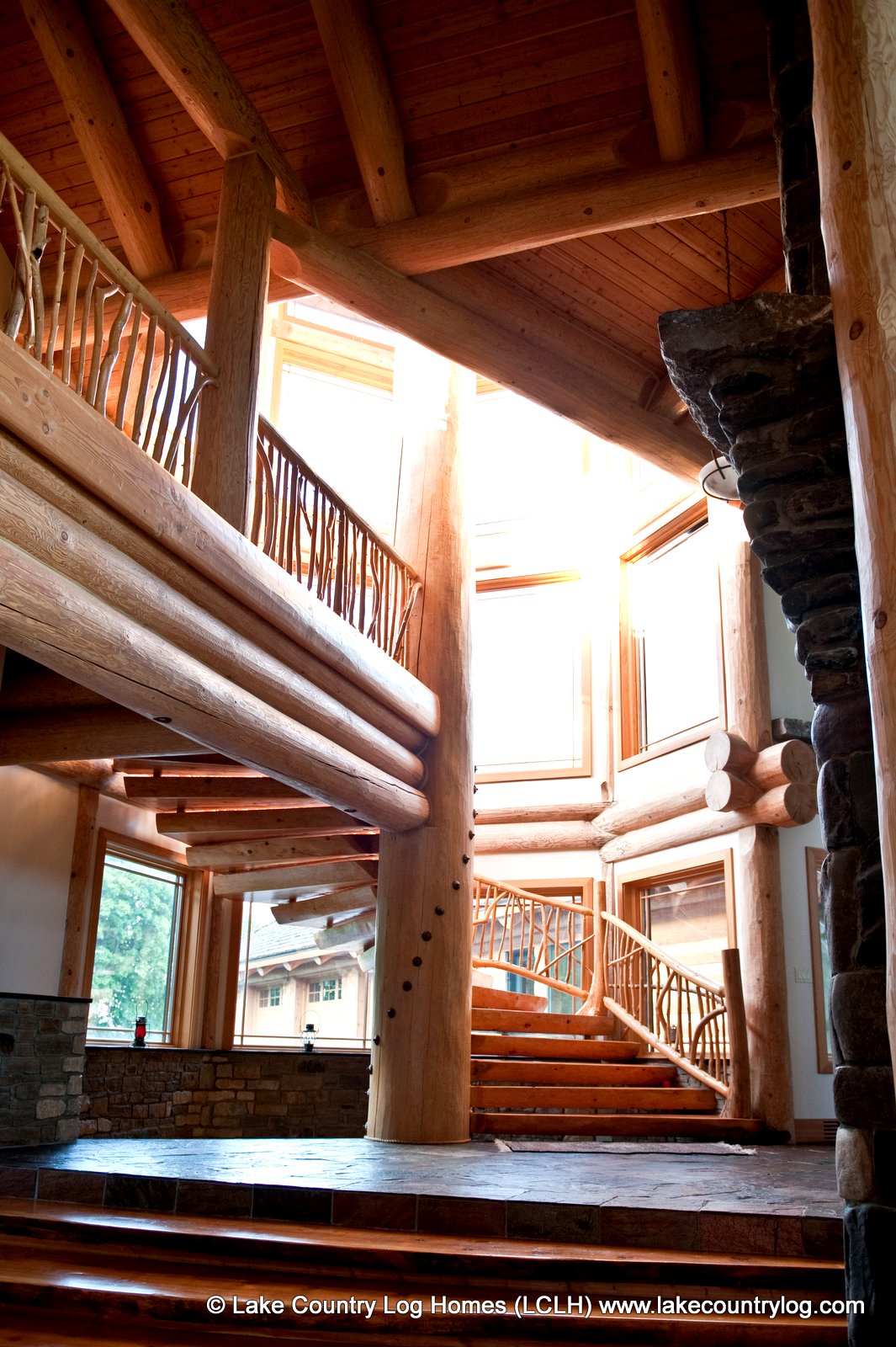 A sculptural timber staircase rising through the stone-and-log interior